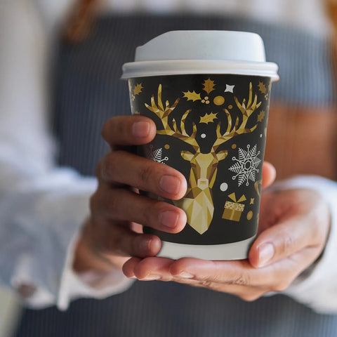 Person holding a coffee cup with a festive design featuring a deer and snowflakes.